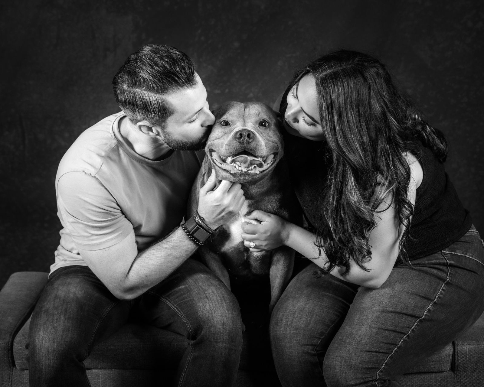 A couple kissing their dog on both cheeks at once