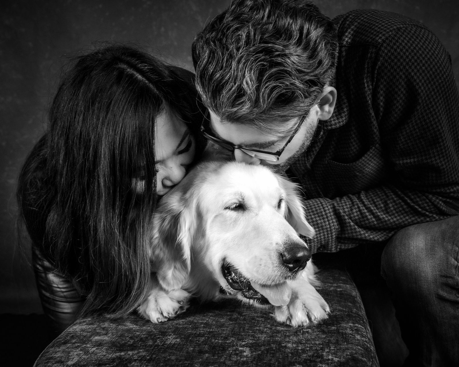 A couple kissing their golden retriever