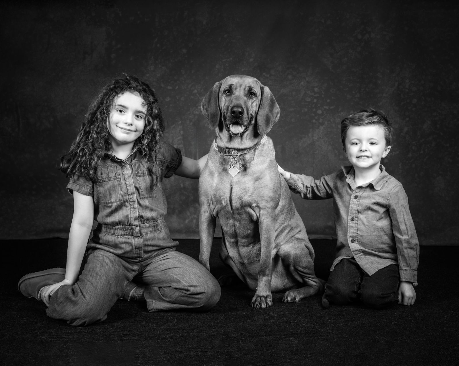 A girl and a little boy on either side of their golden retriever