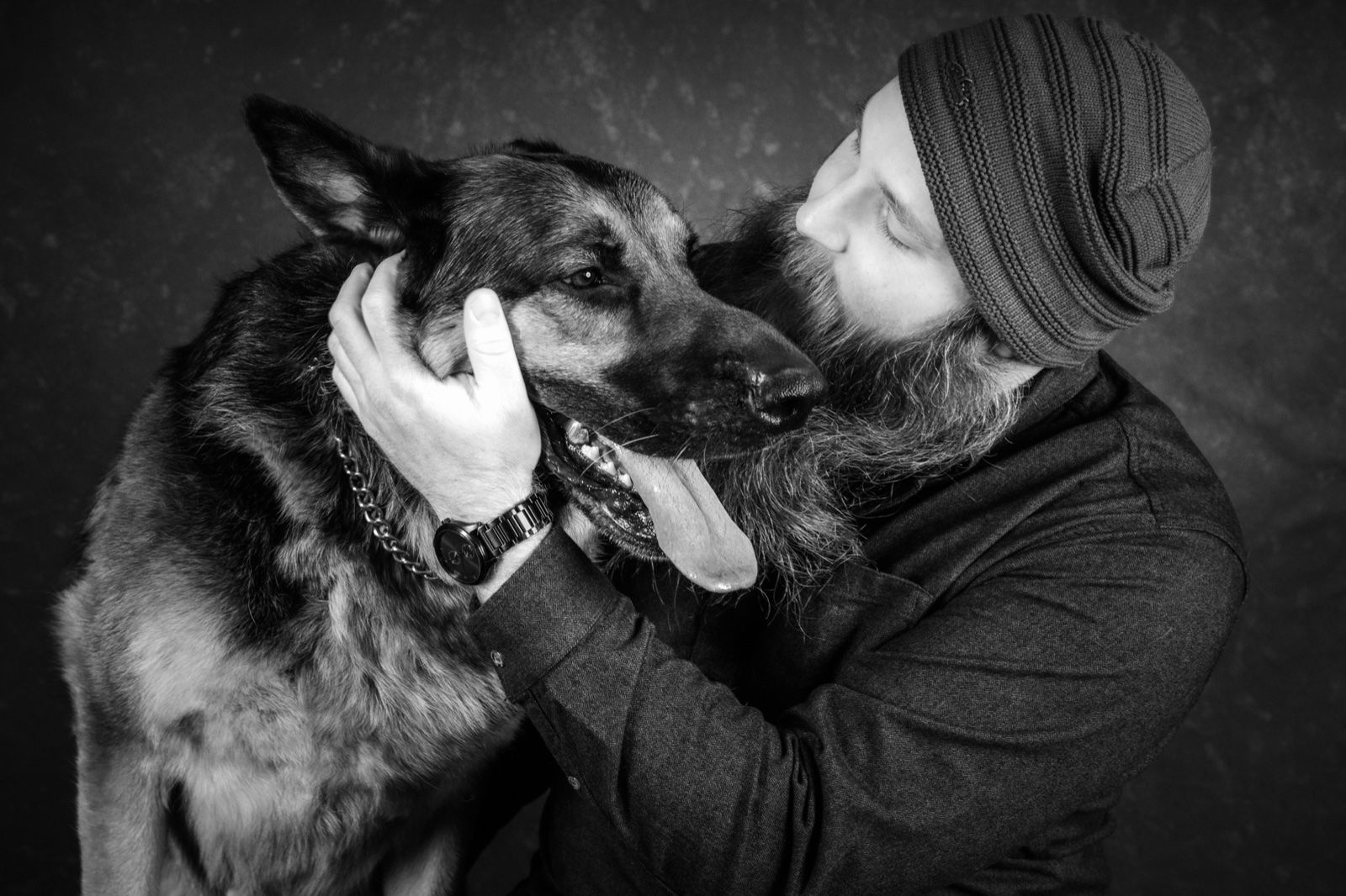 A man in a beanie kissing his German shepherd