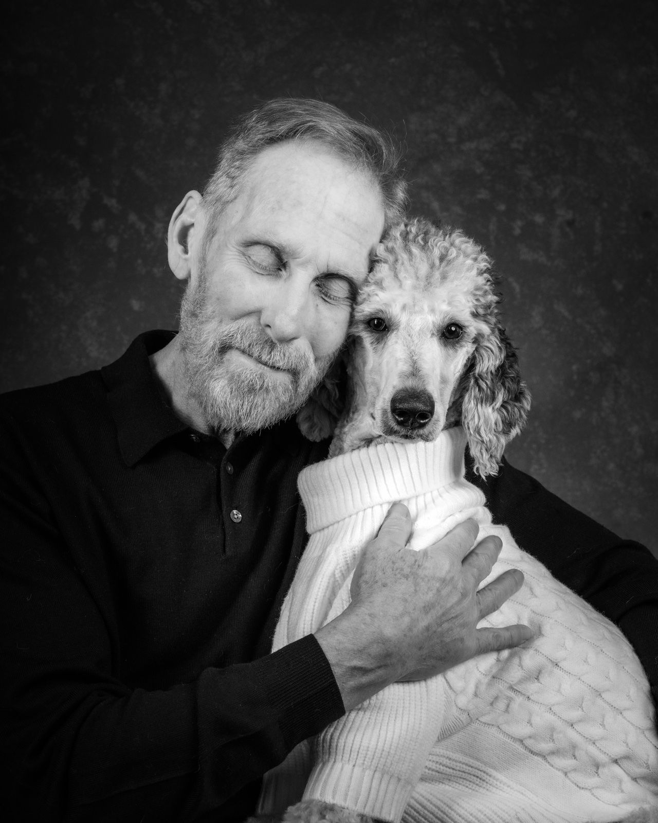 A man with his eyes closed, holding his white poodle close