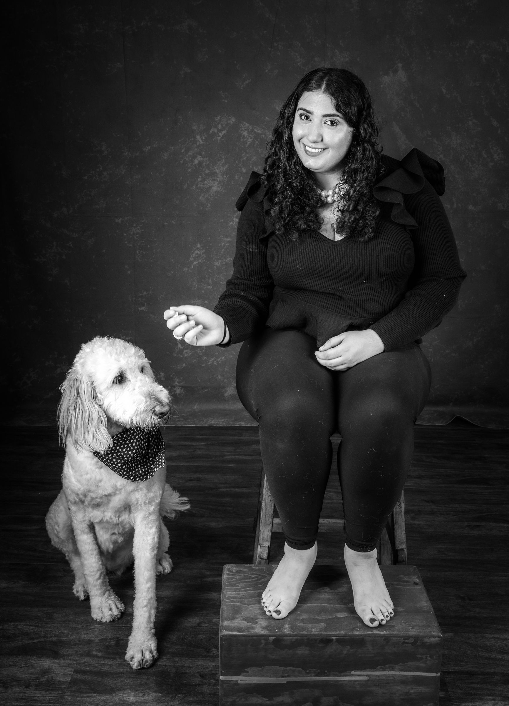 Nadia sitting on the studio stool, her white doodle in a polka-dot bandana sitting beside her and watching her hand
