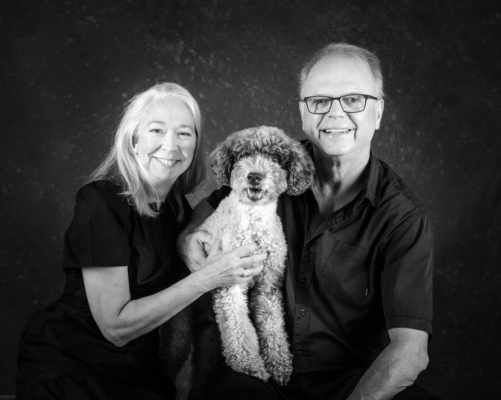 An older couple holding their small poodle