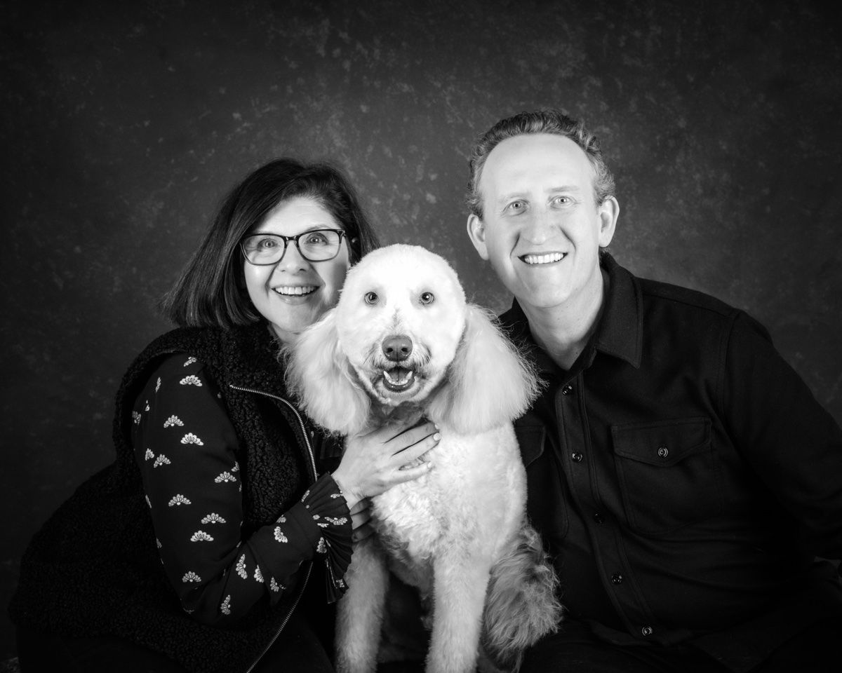 A couple and their white standard poodle, all three looking at the camera