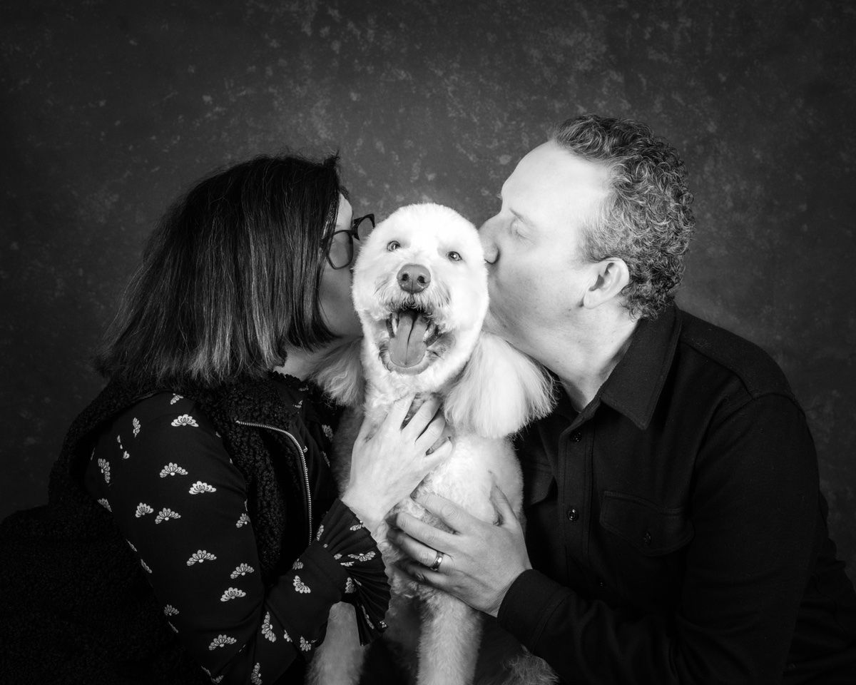 The couple kissing their poodle on both cheeks