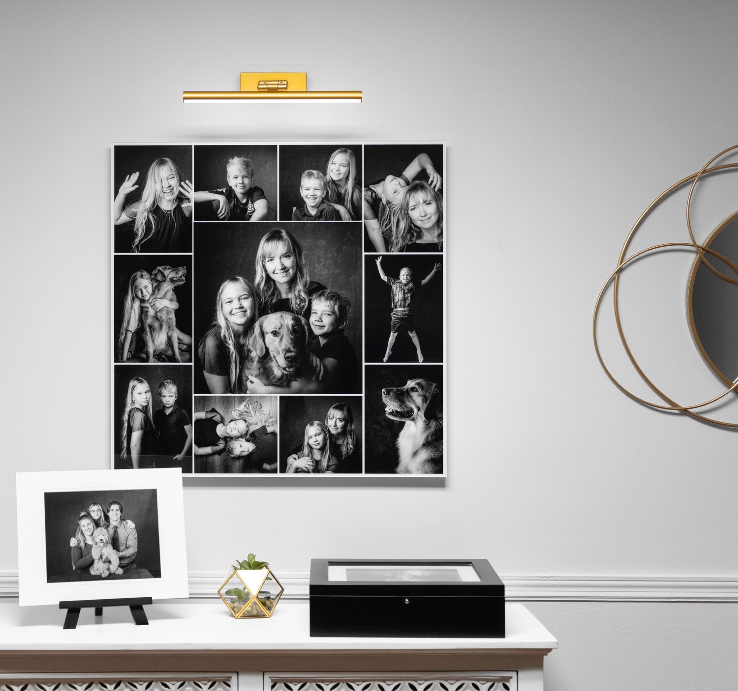 A 30 by 30 inch acrylic collage of a family and their golden retriever on a living-room wall under a brass picture light, a matted print and a portrait box on the console below