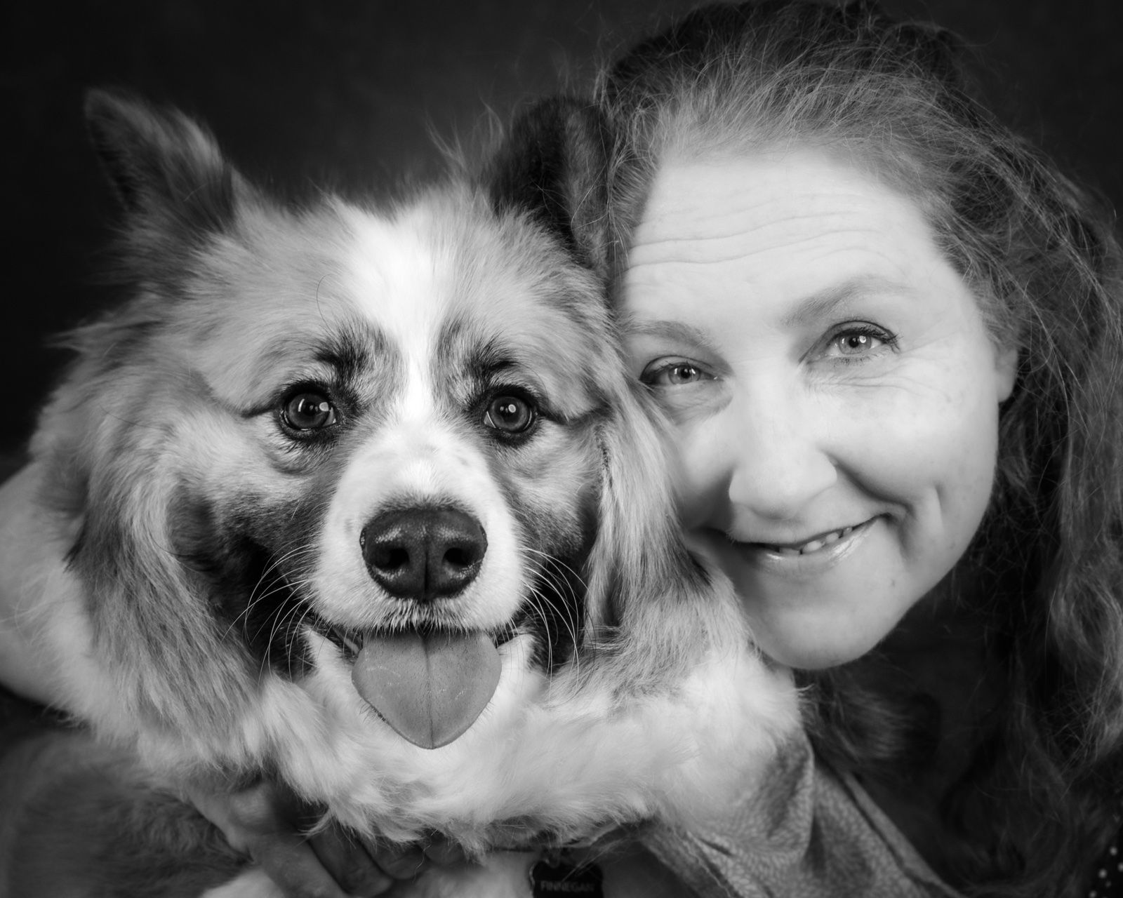 A woman and her fluffy collie mix cheek to cheek, both looking at the camera