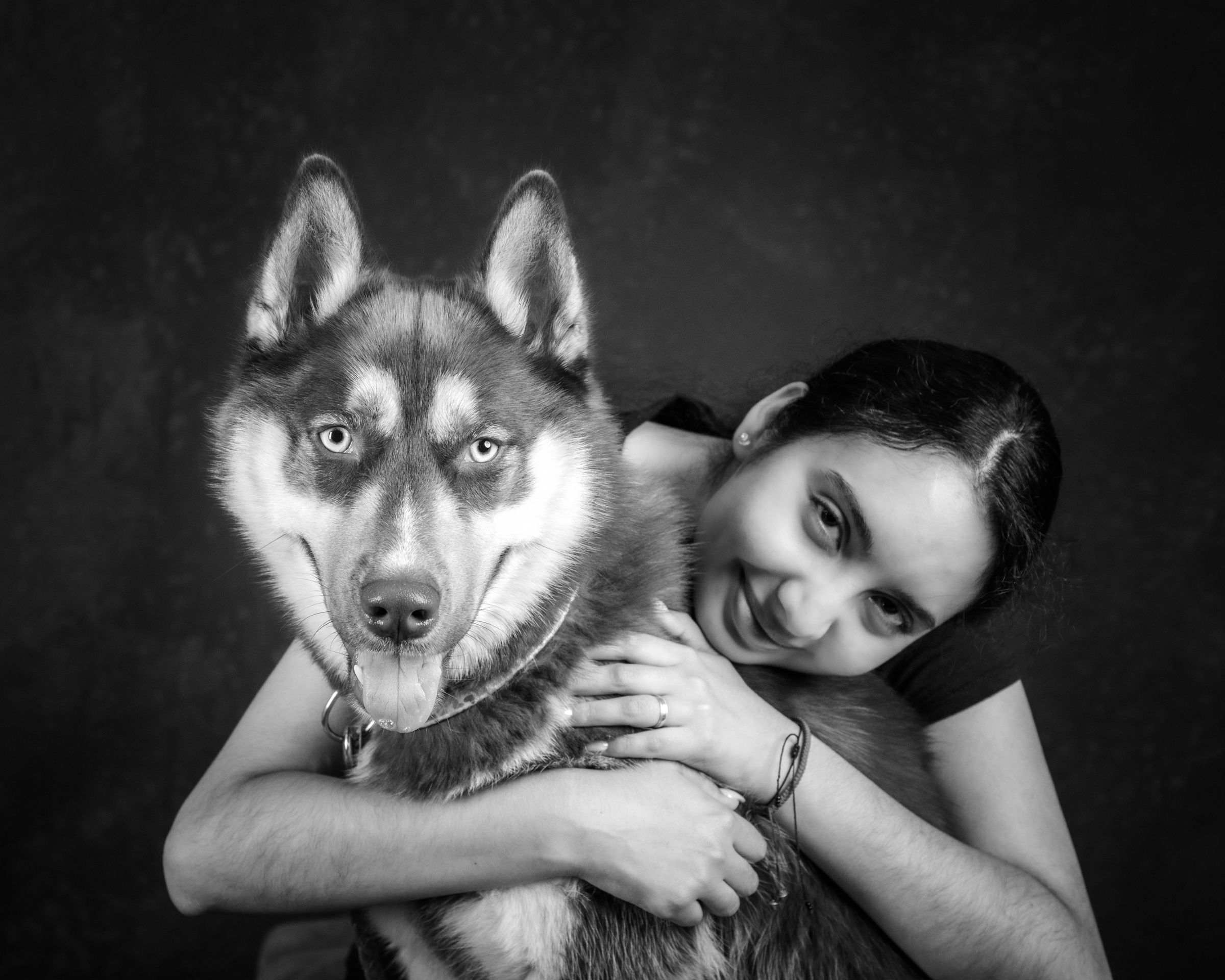 A young woman hugging her husky, both looking at the camera