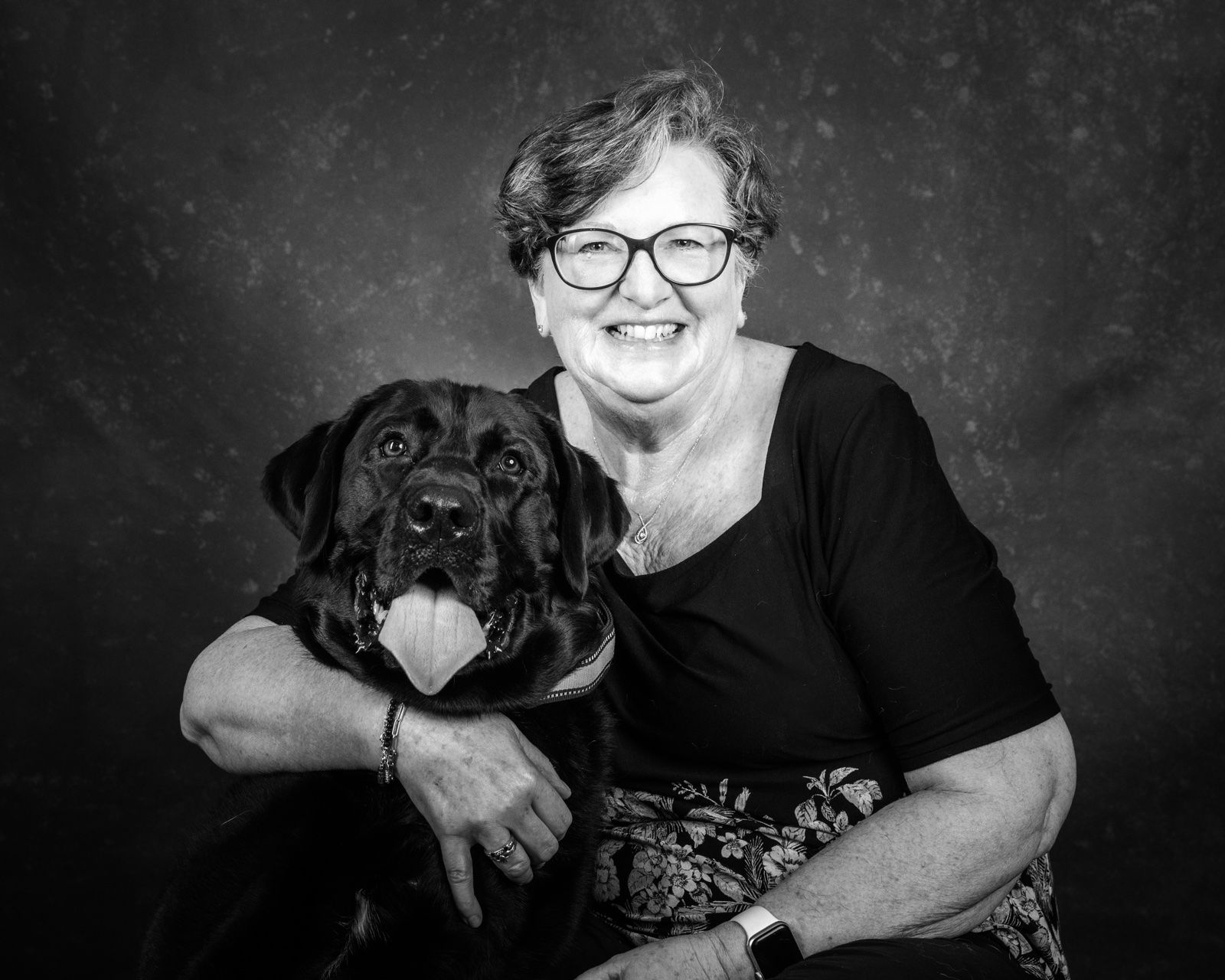 A woman in glasses hugging her rottweiler
