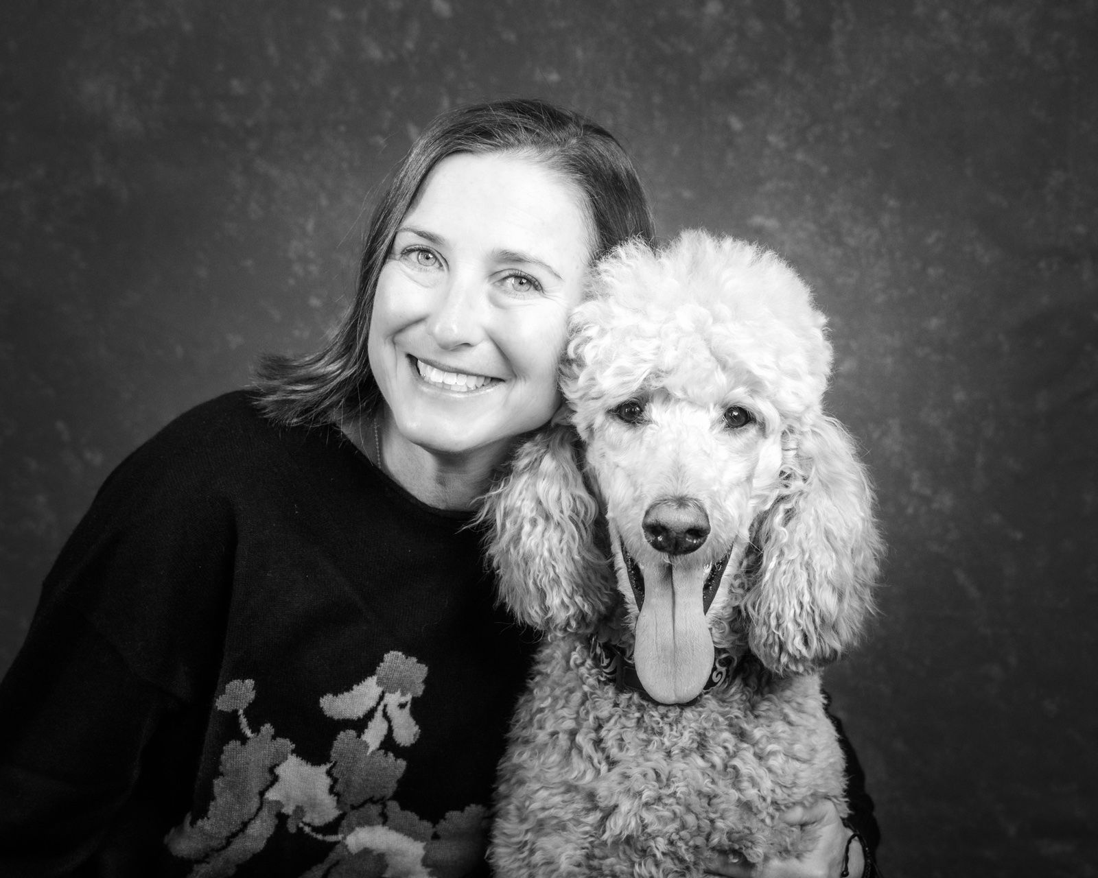 A smiling woman and her standard poodle, cheek to cheek