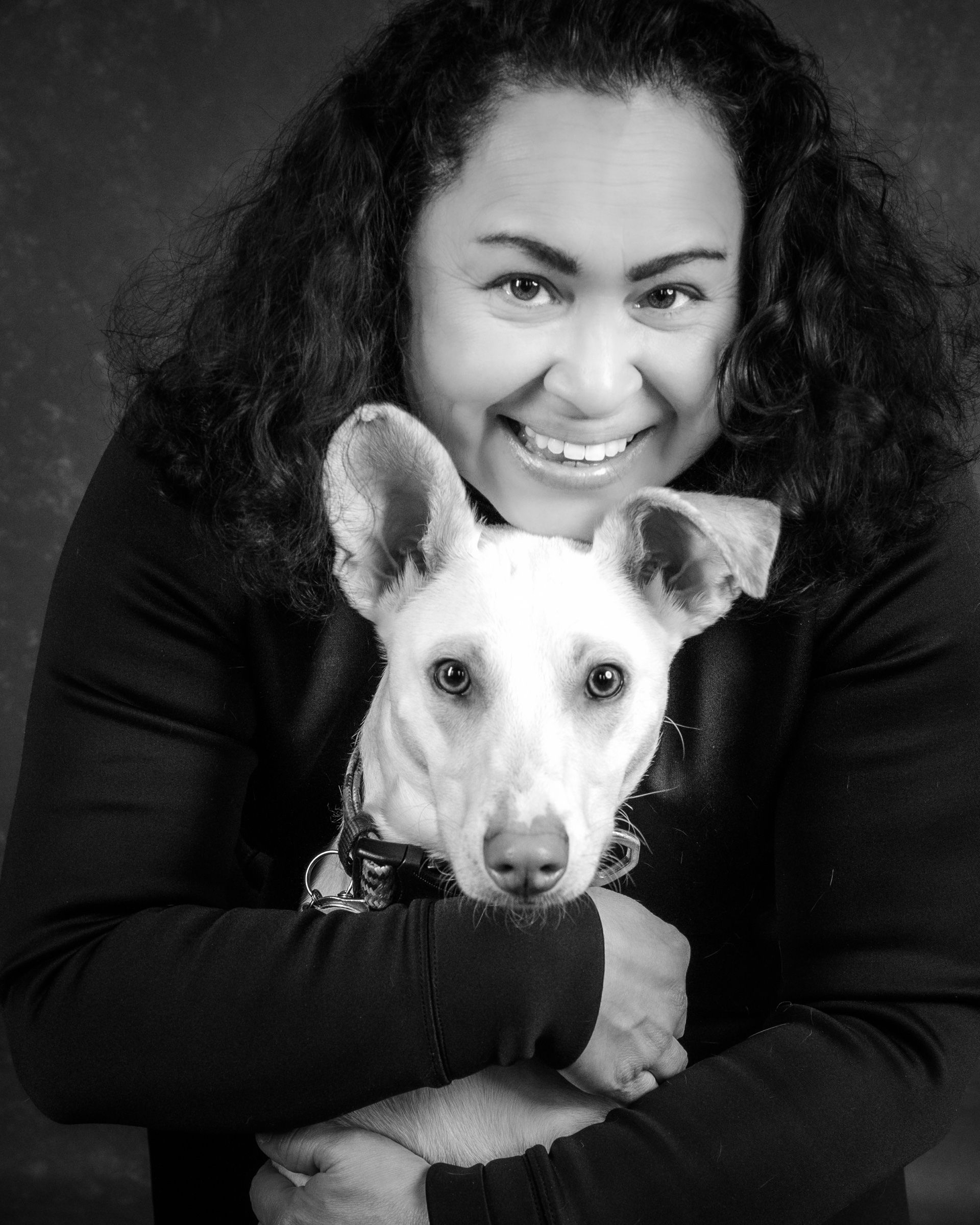 A smiling woman hugging her white dog